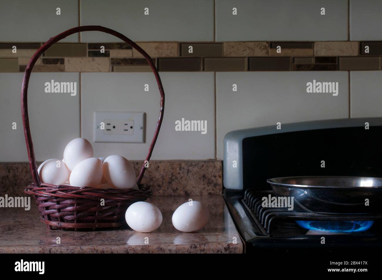 Eine eiserne Pfanne auf dem Kaminfeuer mit einem Korb mit weißen Eiern an der Seite, Konzepte der morgendlichen Mahlzeit Zubereitung in einer Küche, durch ein Fenster Licht beleuchtet Stockfoto