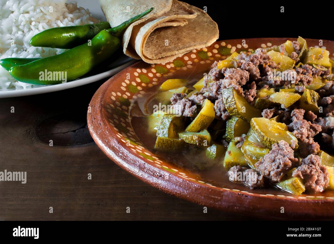 Mexikanische Küche, Picadillo-Fleisch mit Gemüse, Zwiebeln, Paprika und Zucchini, mit einem Teller Knoblauch-Reis auf der Seite, serrano-Chili und Mais-Tortillas. Stockfoto