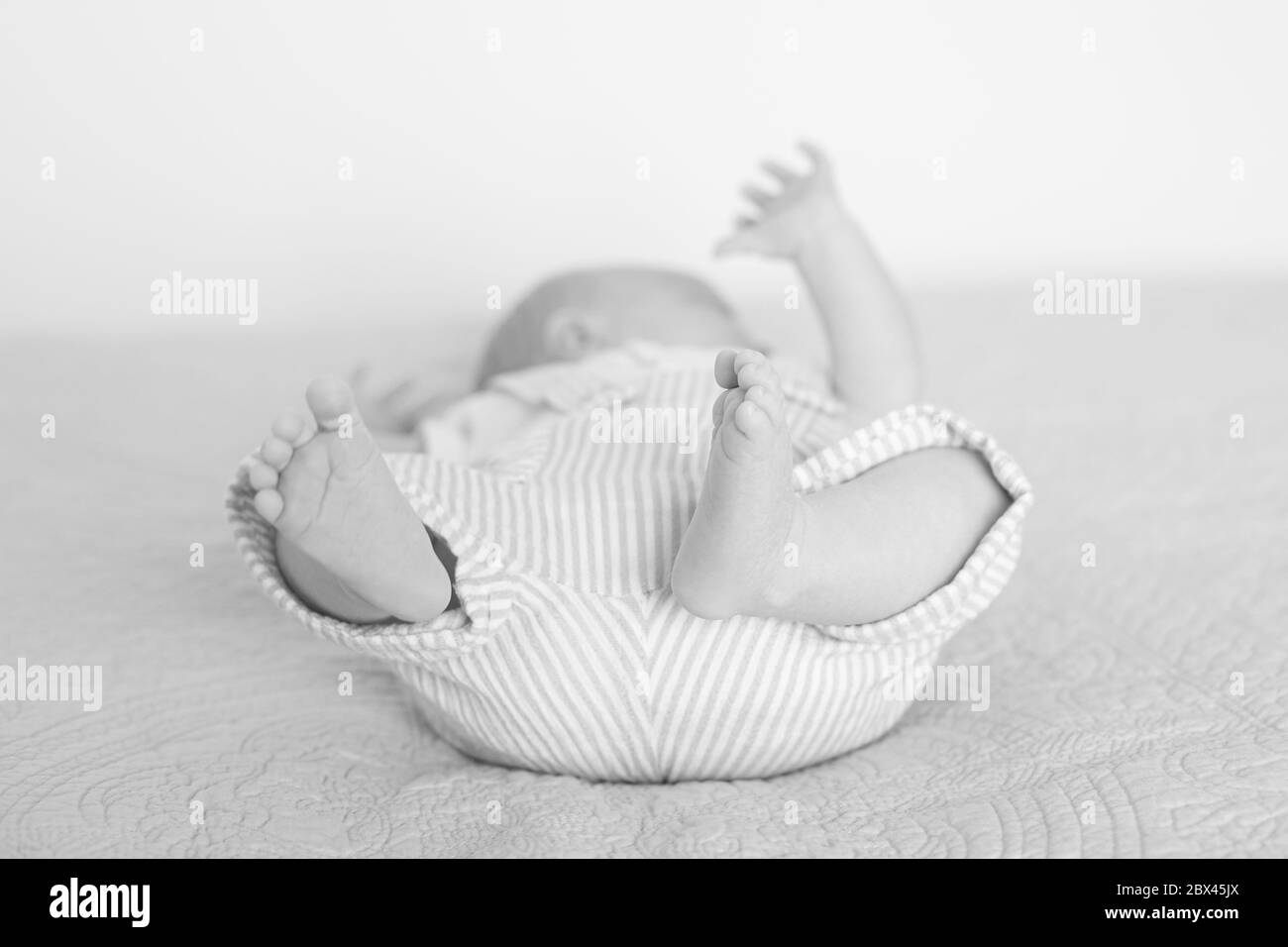Baby liegt auf dem Rücken auf dem Bett drinnen mit den Füßen zu Vordergrund mit Arm nach oben in gestreiften Overalls Stockfoto