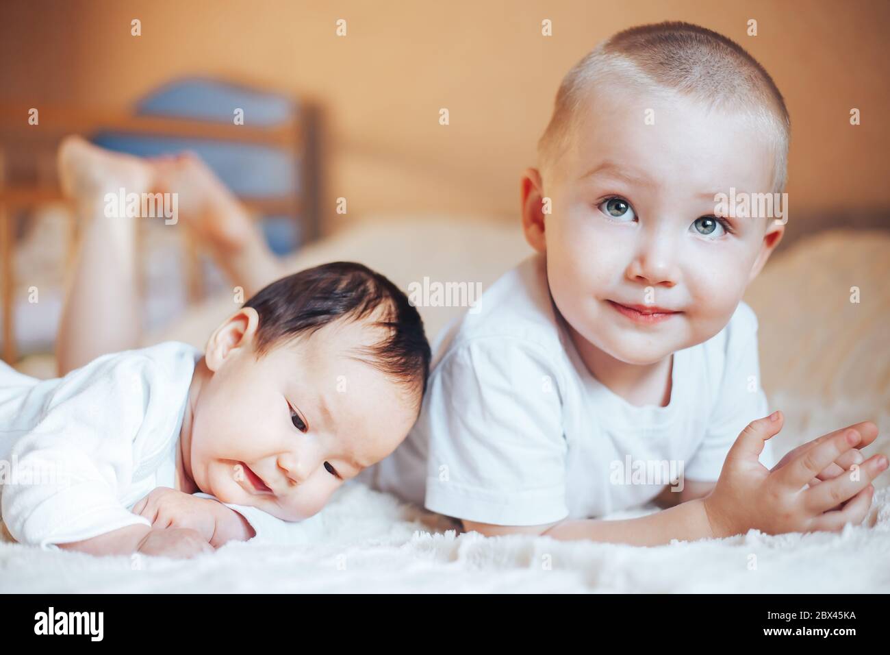 Niedliches kleines Baby mit älterem Bruder, der zu Hause auf dem Bett liegt Stockfoto