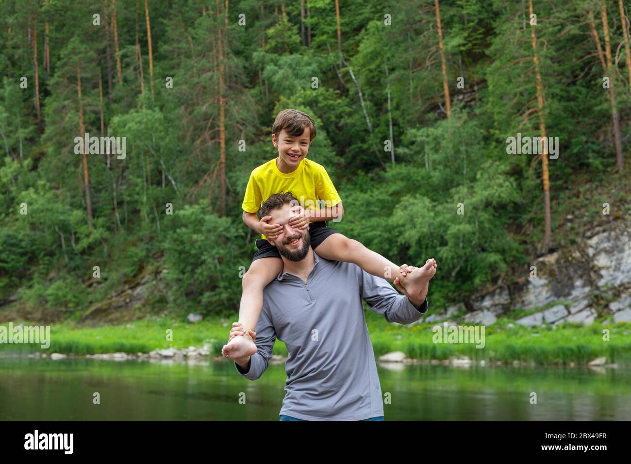 Glücklicher Vater huckepack seinen Sohn draußen. Lachender Junge schloss seine Väter Augen mit den Händen. Stockfoto