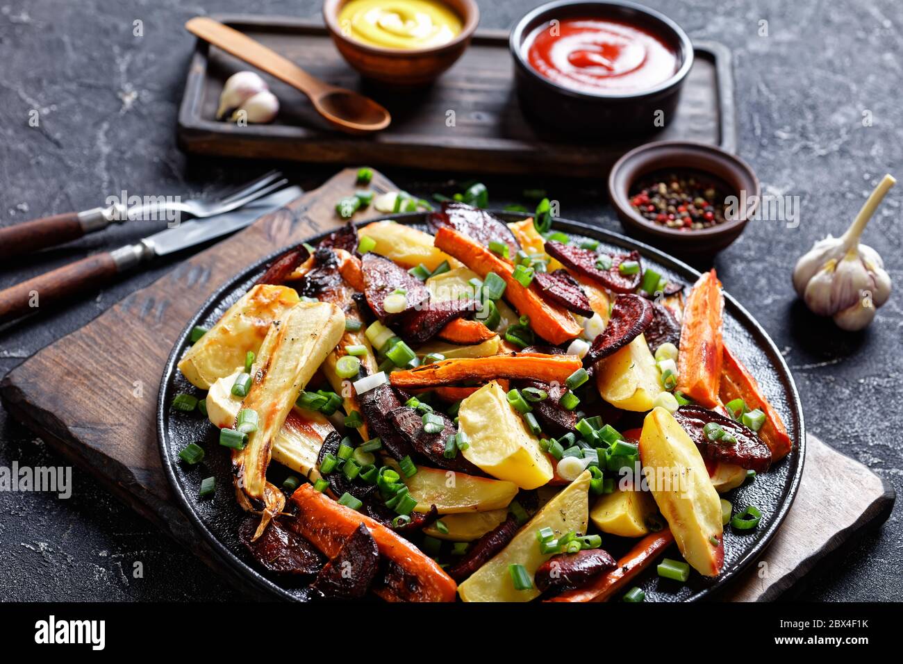 Rote Bete, Kartoffelkeile, Pastinaken, Karotten mit gehackter grüner Zwiebel auf Holzbrett mit Ketchup, Senf, Landschaftsansicht von oben Stockfoto