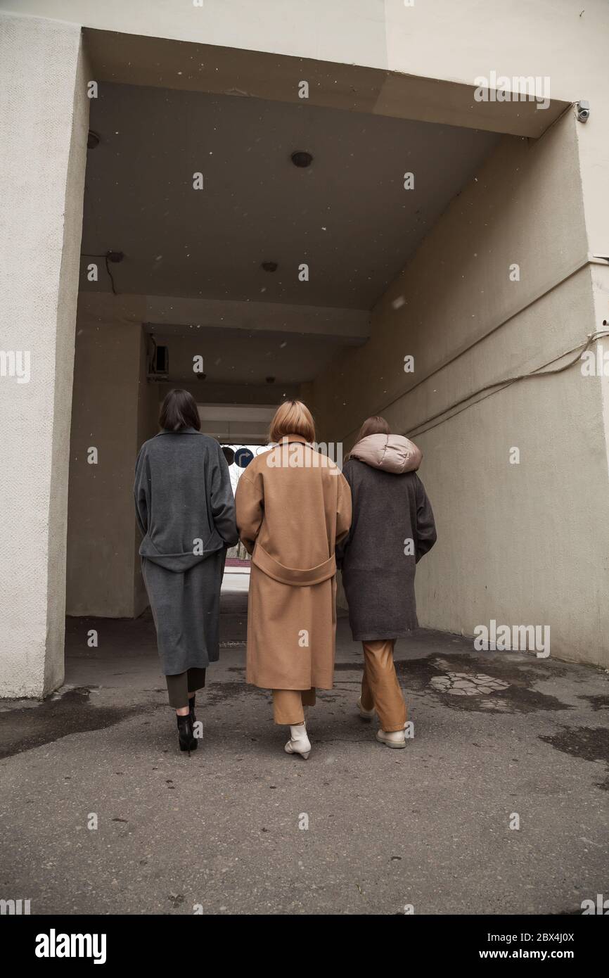 Rückansicht von drei Modellen tragen warme Wollmäntel posiert in Stadt Hintergrund, nicht erkennbar. Low-Winkel-Ansicht. Street-Stil Mode-Bild Stockfoto