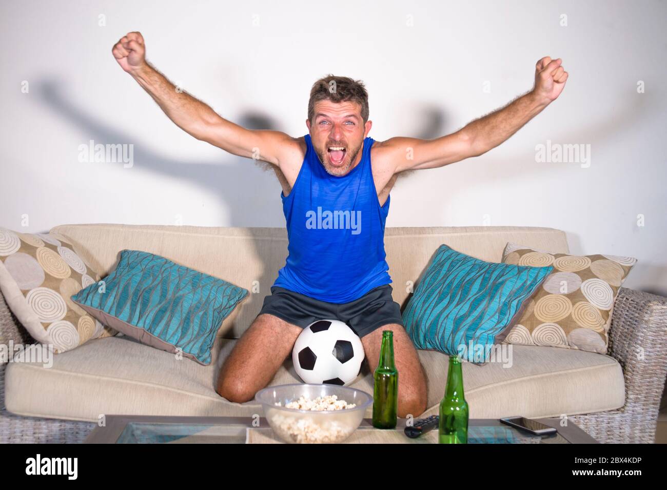 Junge attraktive Mann glücklich und aufgeregt Fußball-Spiel im Fernsehen feiern Siegtreffer verrückt und spastisch mit Bier Popcorn und Fußball in f Stockfoto