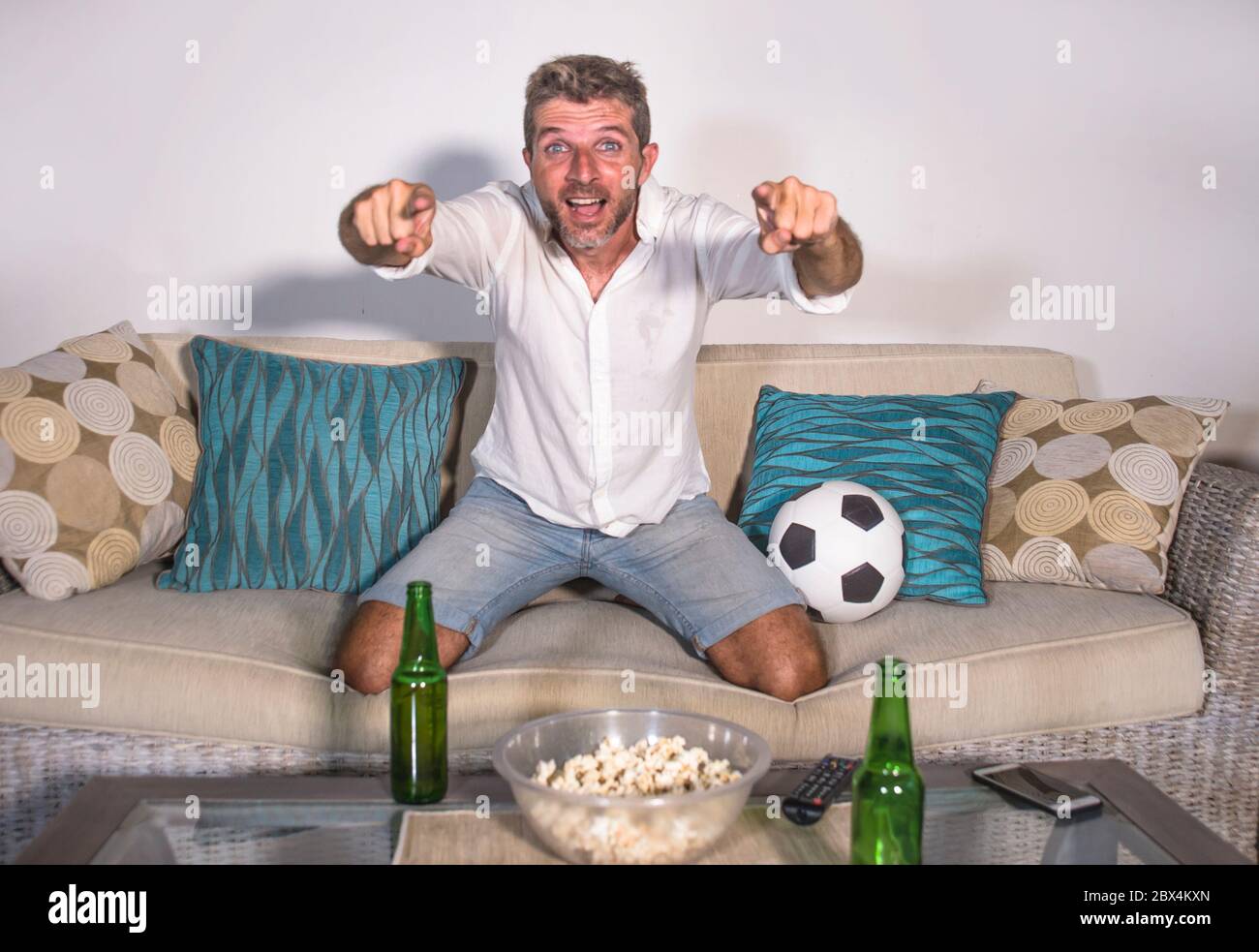 Junge attraktive Mann glücklich und aufgeregt Fußball-Spiel im Fernsehen feiern Siegtreffer verrückt und spastisch mit Bier Popcorn und Fußball in f Stockfoto