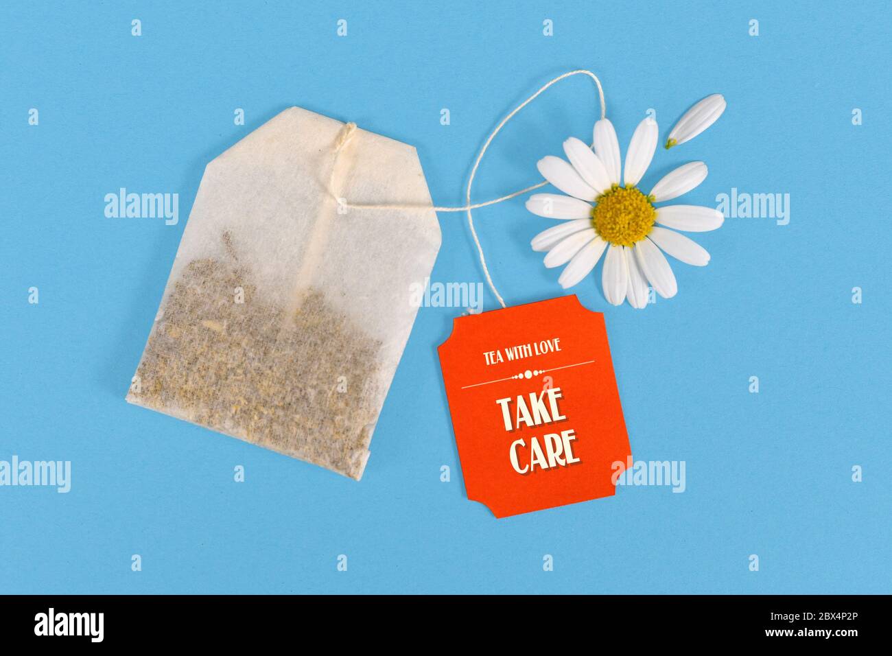 Teebeutel mit niedlichen roten Etikett mit Text 'Take care' mit Gänseblümchen auf blauem Hintergrund Stockfoto
