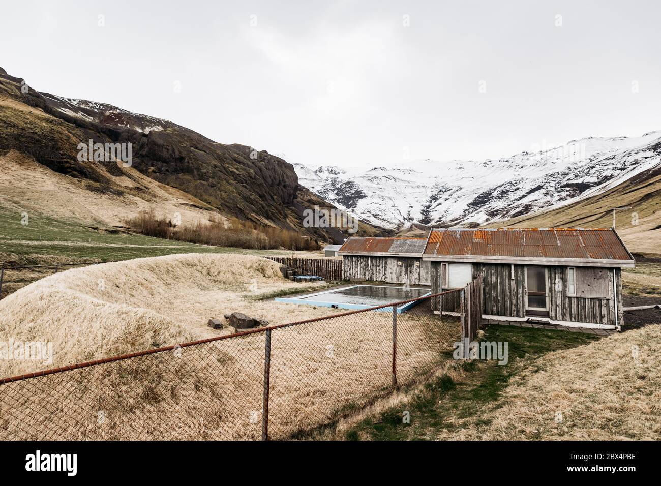 Alte Holzhäuser mit einem Pool von Thermalquellen in Island, vor dem Hintergrund der schneebedeckten Berge. Ein Hotel mit heißen Quellen in den Bergen. Stockfoto