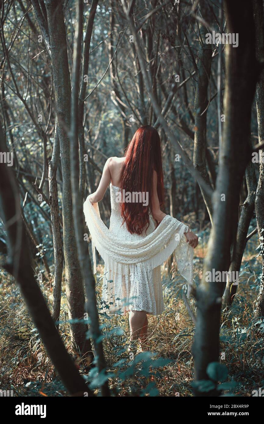 Frau mit langen roten Haaren geht in seltsamen Wald. Ätherisch und romantisch Stockfoto