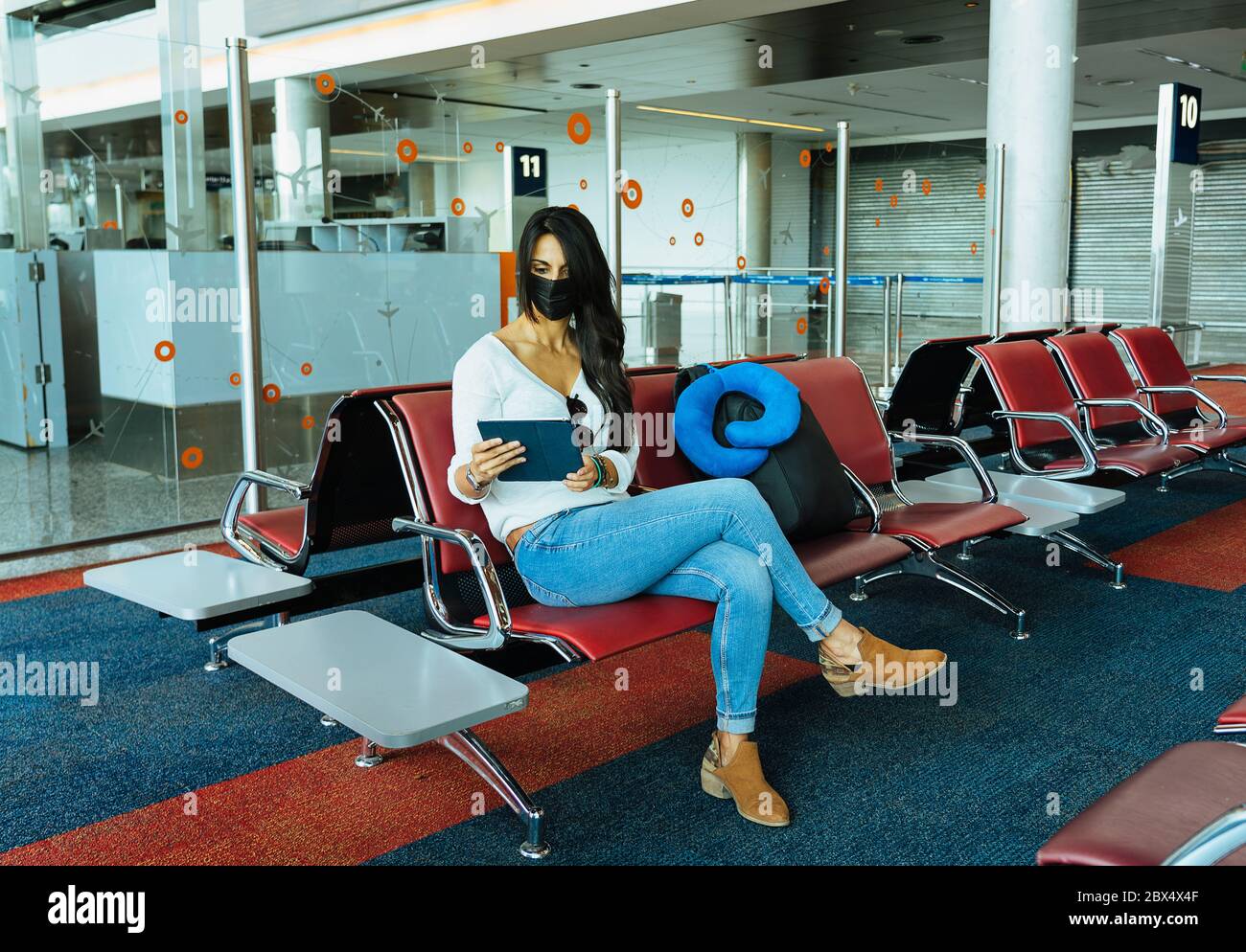 Frau, die ihr Tablet während des COVID-19 Coronavirus auf einem Flughafen mit einer schützenden Gesichtsmaske liest Stockfoto
