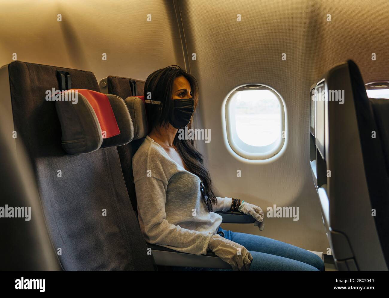 Frau in einem Flugzeug mit Gesichtsmaske Schutz, Coronavirus COVID19 Virus Stockfoto