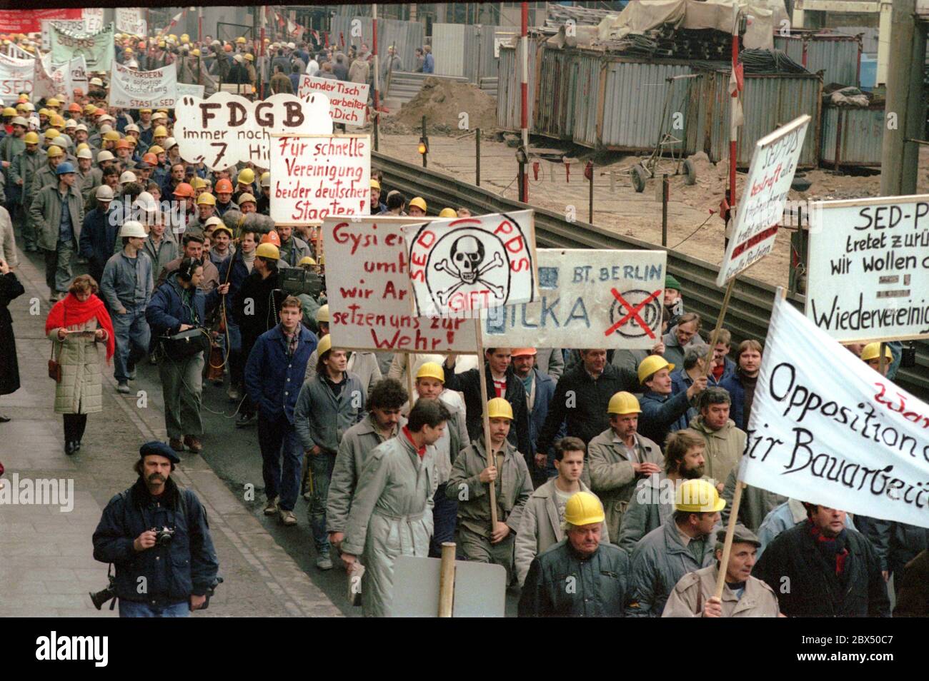 Berlin / DDR / 1990 Bauarbeiter der Friedrichstraße marschieren in die Volkskammer. Der Runde Tisch hat Schwierigkeiten mit der Regierung Modrow (SED/PDS). Sie wollen Druck ausüben. Forderung: Wir wollen Wiedervereinigung. -Keine Stasi, keine SED, sonst verabschiede ich mich von der DDR. - der protestmarsch unter den Linden Forderungen: -für schnelle Vereinheitlichung... / die SED ist Gift. Die SDP war stark in der Firma Ingenieur-Hochbau. Einer der Organisatoren war Knut Herbst (vorne im Trenchcoat), später Abgeordneter des landtags in Berlin / Runder Tisch / DDR / Opposition / Wende Stockfoto