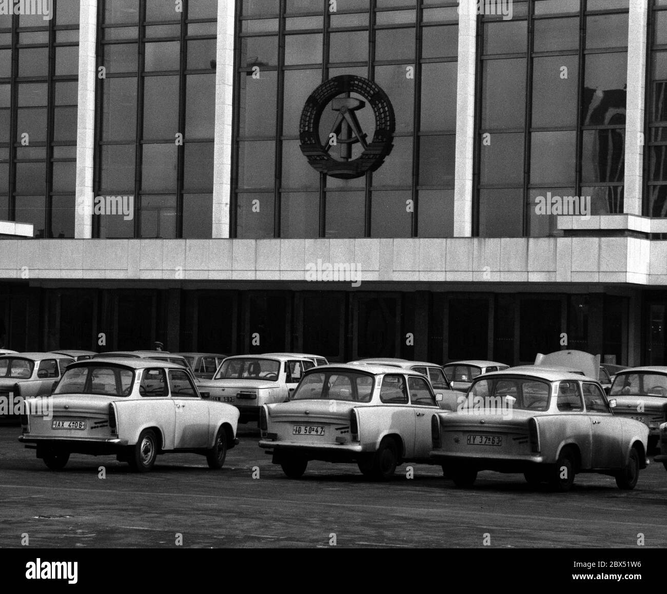 Berliner Bezirke / Ende der DDR / Emblem / 20.2.1985 Ost-Berlin: Palast der Republik. Es gab auch die Volkskammer. Das DDR-Emblem hängt noch immer dort. Der davor abgehngte Parkplatz zeigt den Wohlstand der DDR. Es gab hauptsächlich nur 2 Typen von Autos: Trabant und Wartburg. Der Palast wurde nach der Vereinigung abgerissen. // DDR-Staat / Linden anstelle des 1950 abgerissenen Stadtpalastes wurde ab 1973 das Schloss der Republik gebaut, 180 m lang, 32 m breit. Im Inneren waren verschiedene Einrichtungen. In der großen Halle, die 5000 Besucher hielt, fanden Veranstaltungen statt. Die Volkskammer der DDR Stockfoto