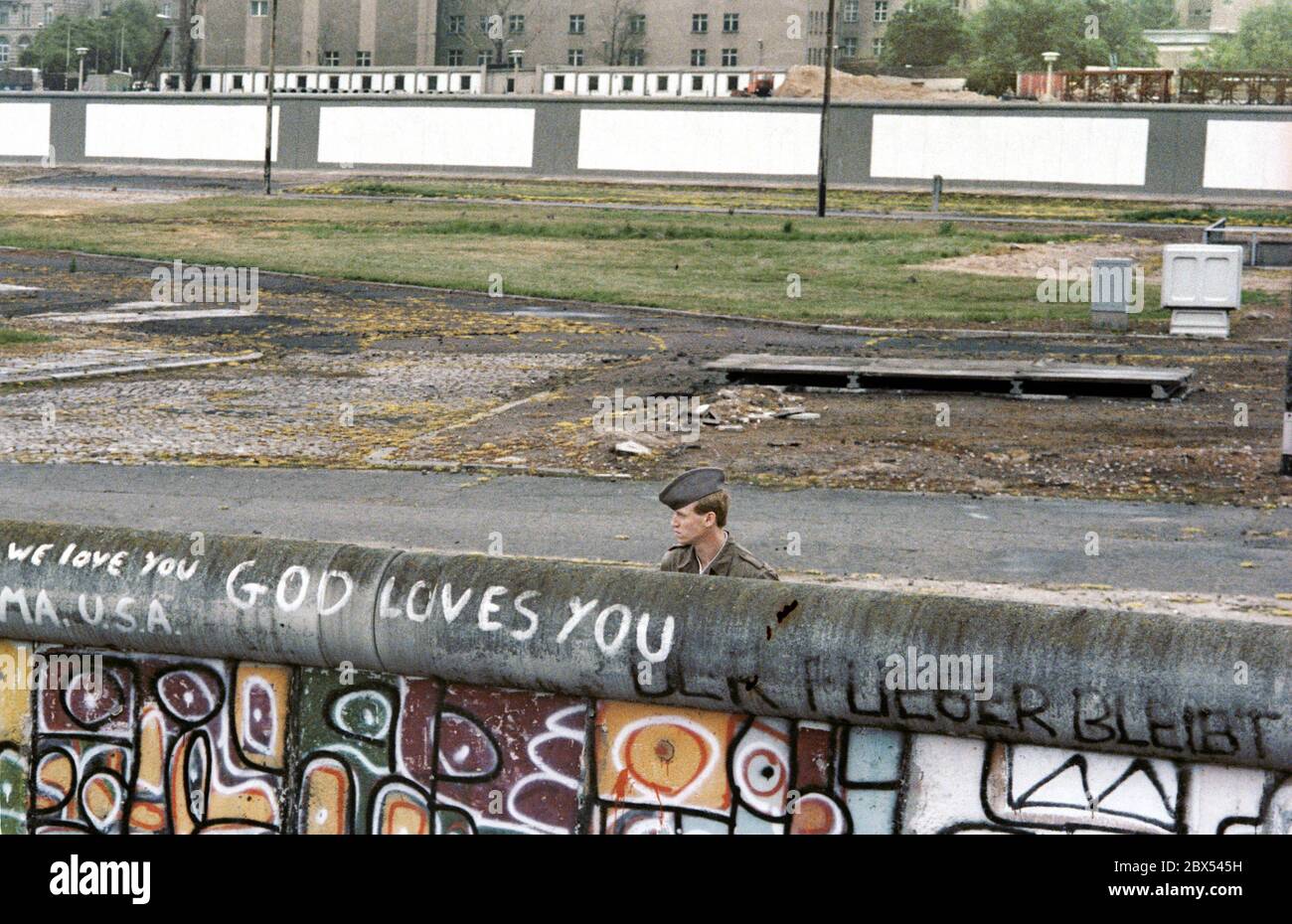 Berlin-City / Mitte / DDR / 6 / 1988 Potsdamer Platz: DDR-Grenzposten blicken nach West-Berlin. Junge Leute haben dort ein Stück Niemandsland besetzt. Sie liegt im Westen, gehört aber zum Osten. Die West-Berliner Polizei ist dabei, evakuiert zu werden. Der DDR-Grenzschutz weiß nicht, was auf der Westseite der Mauer steht: -Gott liebt dich- // DDR-Mauer / Geschichte / Kommunismus / DDR-Staat [automatische Übersetzung] Stockfoto