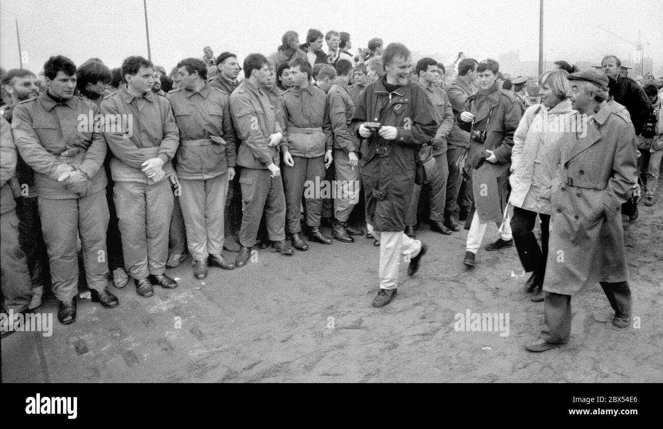 Berlin-City / Mitte / Berliner Mauer 12.11.1989 Potsdamer Platz: Es gibt eine Lücke in der Mauer, Menschen kommen aus Ost- und Westberlin. Die Einheit der DDR-Grenzposten mit ihren Kalaschnikows erschreckt niemanden mehr. Sie gehören zur STASI-Einheit von Feliks Dscherschinski. Nach dem Gründer des sowjetischen Geheimdienstes Tscheka. Ein Offizier weist DDR-Bürgern den Weg nach Westen. Es gibt eine Verteidigungslinie für DDR-Bürger, die nach Westen fahren. // Vereinigung / Mauerende / DDR / Volksarmee / Grenzposten / Geschichte / Kommunismus Stockfoto