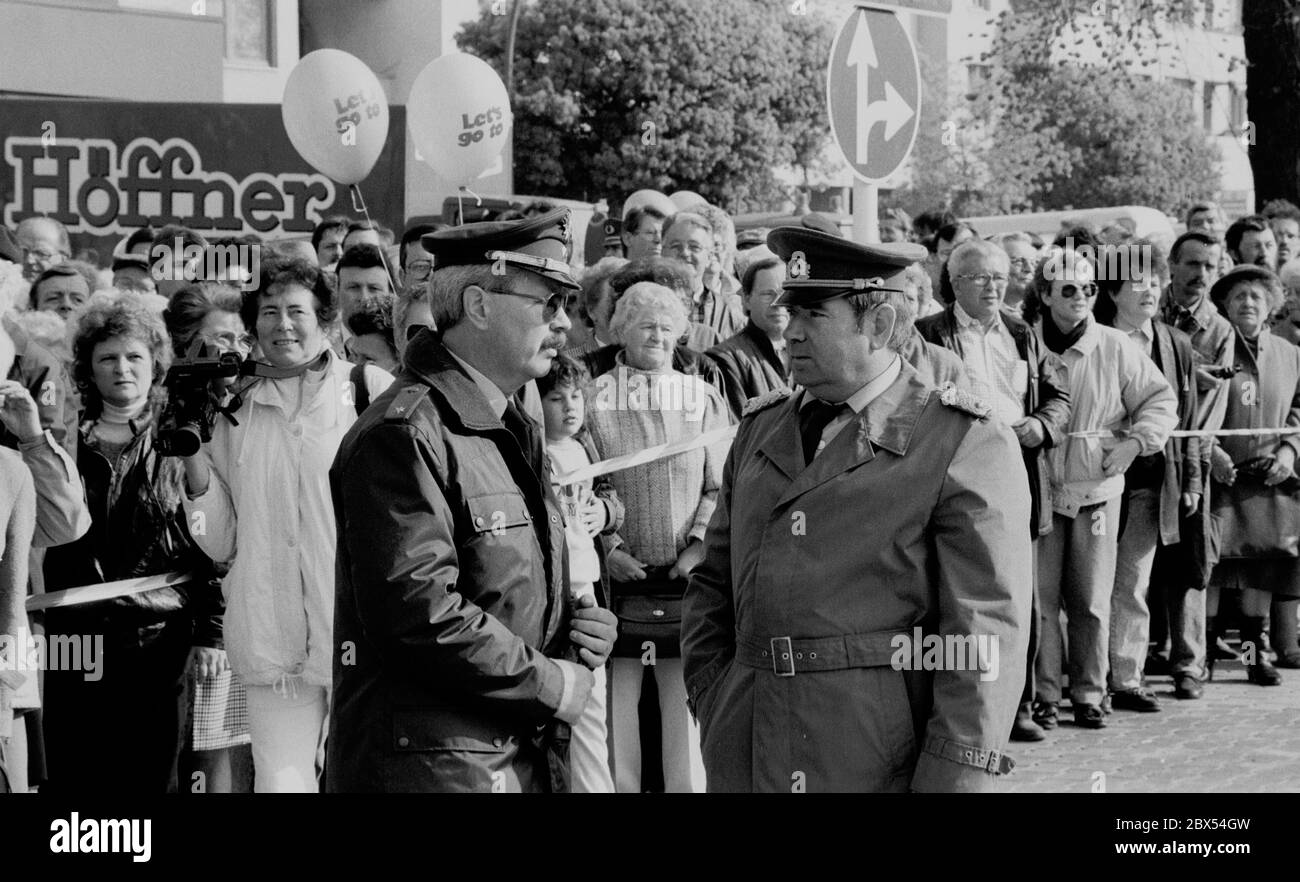 Berlin / Hochzeit / Mitte / Bernauer Strasse 1990 die Mauer fällt ! Am 12. Juni 1990 in Berlin-Wedding, Bernauer Straße. Beim Mauerbau 1961 sprangen Menschen aus den Fenstern auf den Bürgersteig, um nach West-Berlin zu gelangen. Jetzt ist die Grenze weg. Im Vordergrund, ein DDR-Grenzposten und ein West-Berliner Polizist, regeln sie den Verkehr. // Berliner Mauer / [automatisierte Übersetzung] Stockfoto