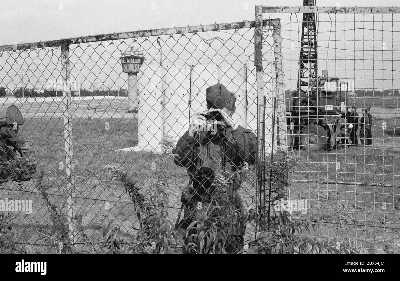 Berlin-Neukölln / DDR / Mauer 8 / 1979 die Mauer wird am Toepchiner Weg erneuert. Die DDR ersetzt die alten Betonplatten durch L-förmige Normelemente, die Todesstreifen sind ebenfalls standardisiert. Ein DDR-Grenzposten bewacht die Bausäule und fotografiert alles auf der Westseite. Die Grenztruppen standen unter der Kontrolle der Stasi // Geschichte / Fotografen / Staat / Bezirke Stockfoto
