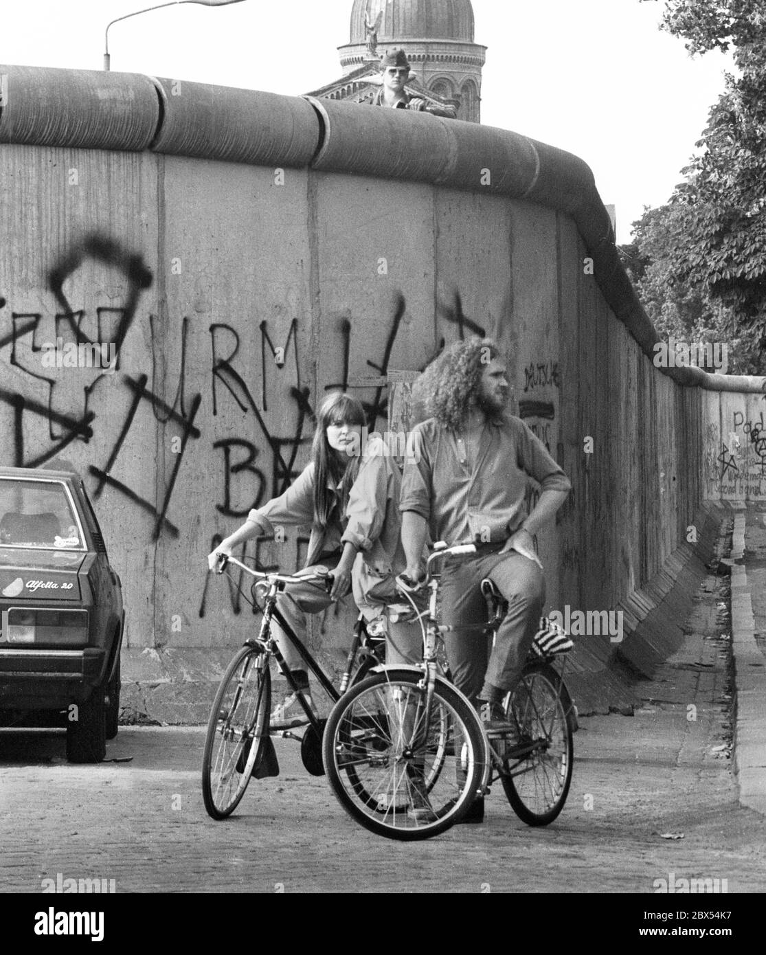 Berliner Stadtteile / Mauer / Kreuzberg / Mitte/ 1983 Legiendamm, davor zwei typische Bewohner des Alternativbezirks, über einem DDR-Grenzposten blickt über die Mauer // DDR / Grenze / [automatische Übersetzung] Stockfoto