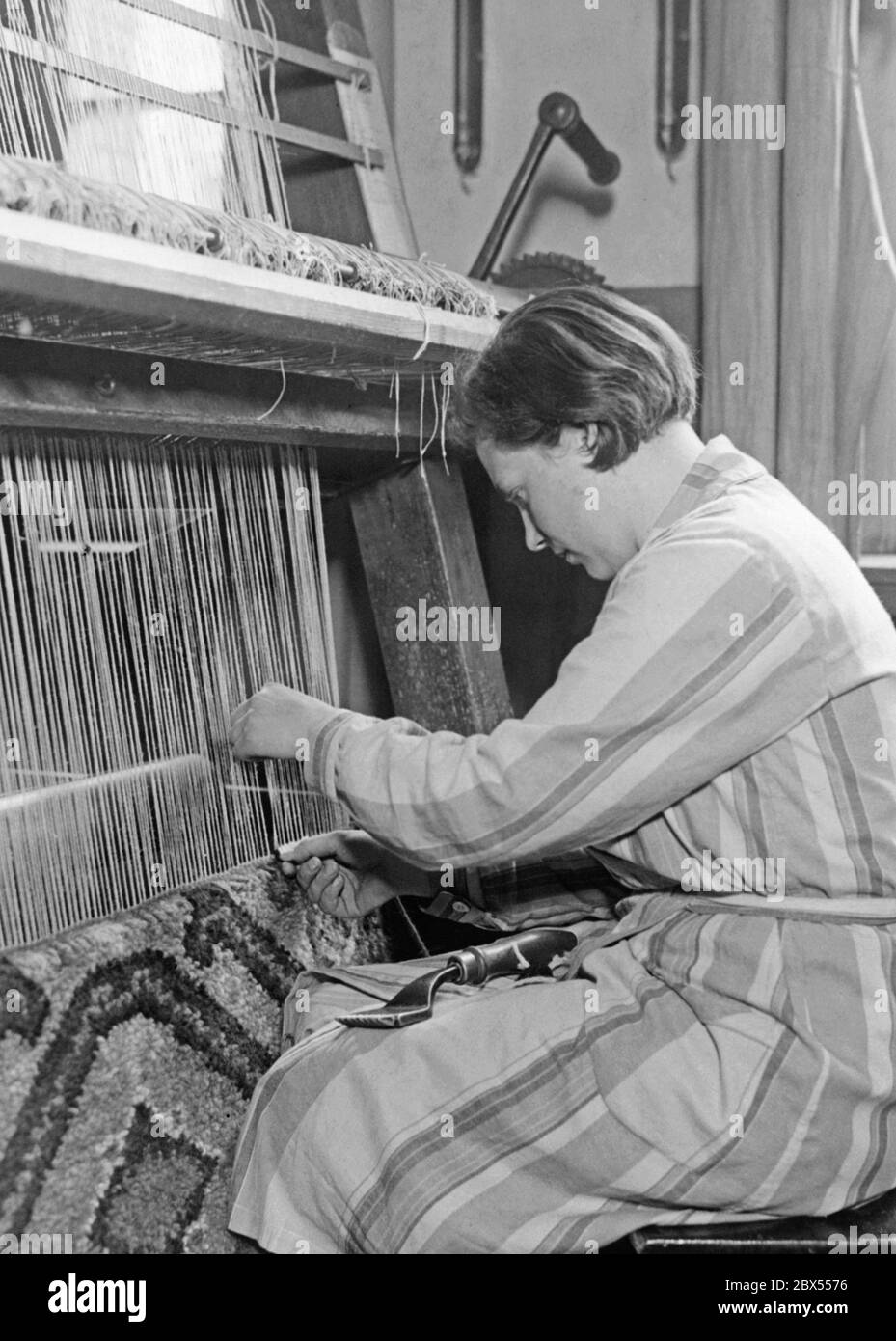 Ausbildung an einer höheren kommunalen Fachschule für Textilhandel oder auch 'Schule of Fashion': Hier lernt ein Auszubildender die Technik des Verknotens von Teppichen auf einer Teppichknüpfmaschine. Stockfoto