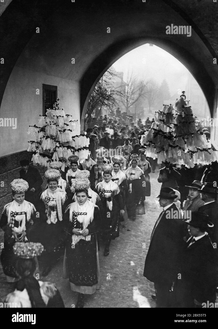 Das Bild vom 6. Februar 1929 zeigt eine Hochzeitsprozession mit Maibästen auf dem Weg zur Kirche. Die Frauen tragen traditionelle Trachten und Brautkränze (Schaeppel). Stockfoto
