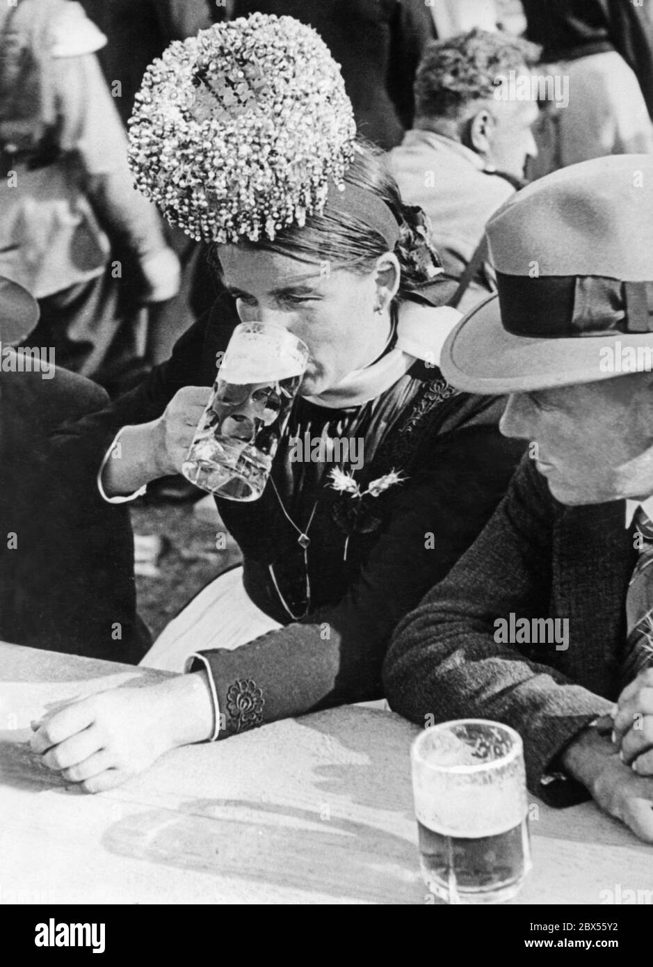 Eine Frau trägt ein festliches Tracht mit einer Schäppel (Brautkrone) und trinkt beim Erntefest im Schapbachtal im Schwarzwald Bier. Dieses Bild wurde wahrscheinlich in den 1930er Jahren aufgenommen. Stockfoto