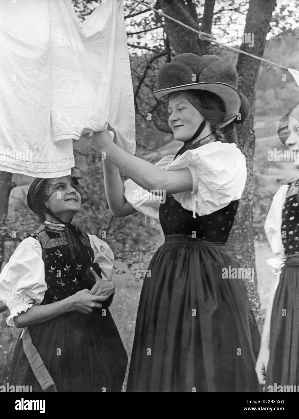 Drei Mädchen aus dem Gutachtental im Schwarzwald in Tracht beim Aufhängen ihrer Wäsche. Das Mädchen in der Mitte des Bildes trägt eine Bollenhütte. Das Bild wurde wahrscheinlich in den 1930er Jahren aufgenommen. Stockfoto