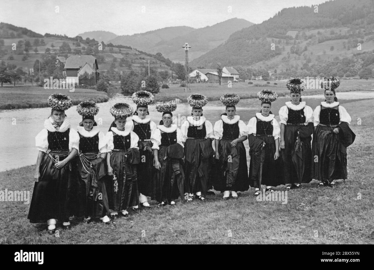 Das Foto von 1930 zeigt eine Reihe von Mädchen und jungen Frauen aus dem Kinzigtal im Schwarzwald in ihren festlichen Kostümen mit Schaeppel-Krone. Im Hintergrund das Kinzigtal mit Bauernhäusern und Wiesen. Stockfoto