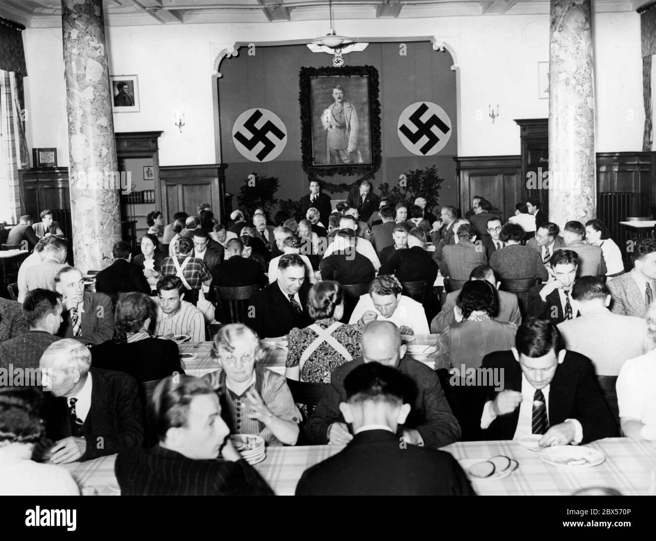 Blick in die Kantine des Hauses für die Rückkehrer der ausländischen Organisation der NSDAP während des Mittagessens. An der Wand zwischen zwei Hakenkreuzen ist ein Porträt von Adolf Hitler zu sehen. Stockfoto