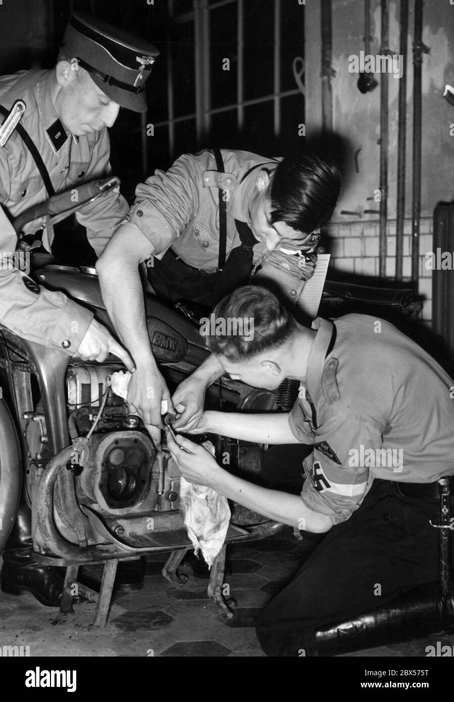 Mitglieder der Hitlerjugend während einer Lektion über den Bau eines Motors. Die Jugendlichen zerlegen den Motor einer BMW-Maschine. Das Motorrad ist wahrscheinlich ein BMW R12. Ein NSKK-Mitglied hilft ihnen. Stockfoto