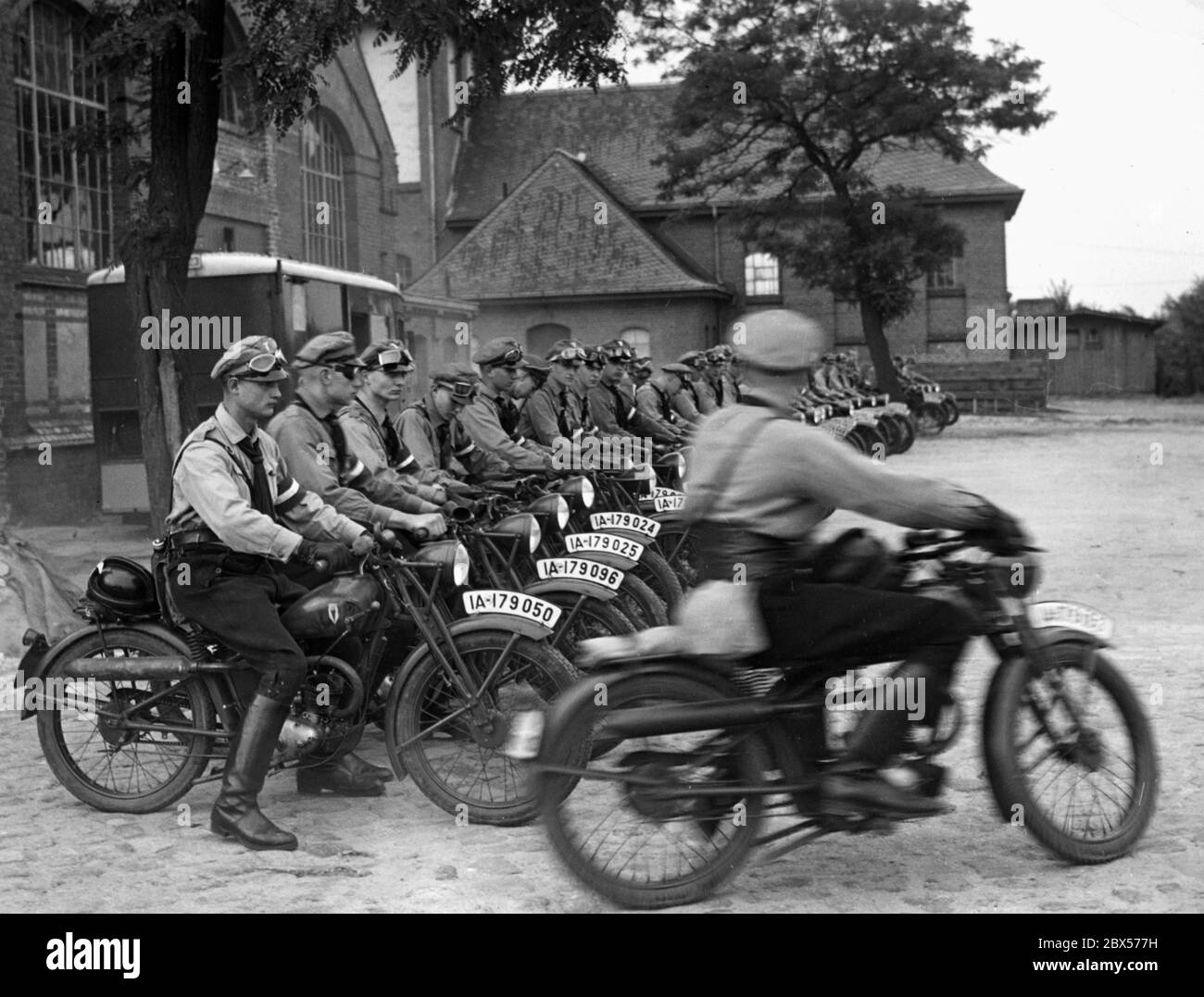 Eine Gruppe der Motor-Hitler-Jugend steht auf ihren Motorrädern an und ist dabei, Lichterfelde nach Goslar zu verlassen. Die Motorräder, auf denen sie sitzen, sind vom Typ DKW RT 98 ccm. Im Hintergrund befindet sich eine Wasserpumpstation. Stockfoto