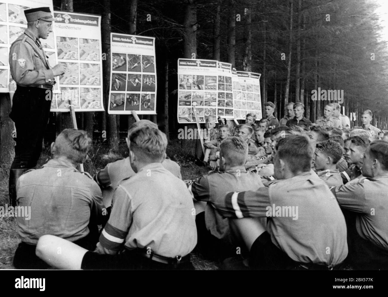 Am Potsdamer Platz in der Nodoer Heide erhalten Mitglieder der Motor-Hitler-Jugend eine theoretische Ausbildung in Verkehrsordnung. An den Bäumen sind Lehrtafeln angebracht. Die Jugendlichen sitzen um sie herum, während ein SA-Mann die Lektionen leitet. Stockfoto