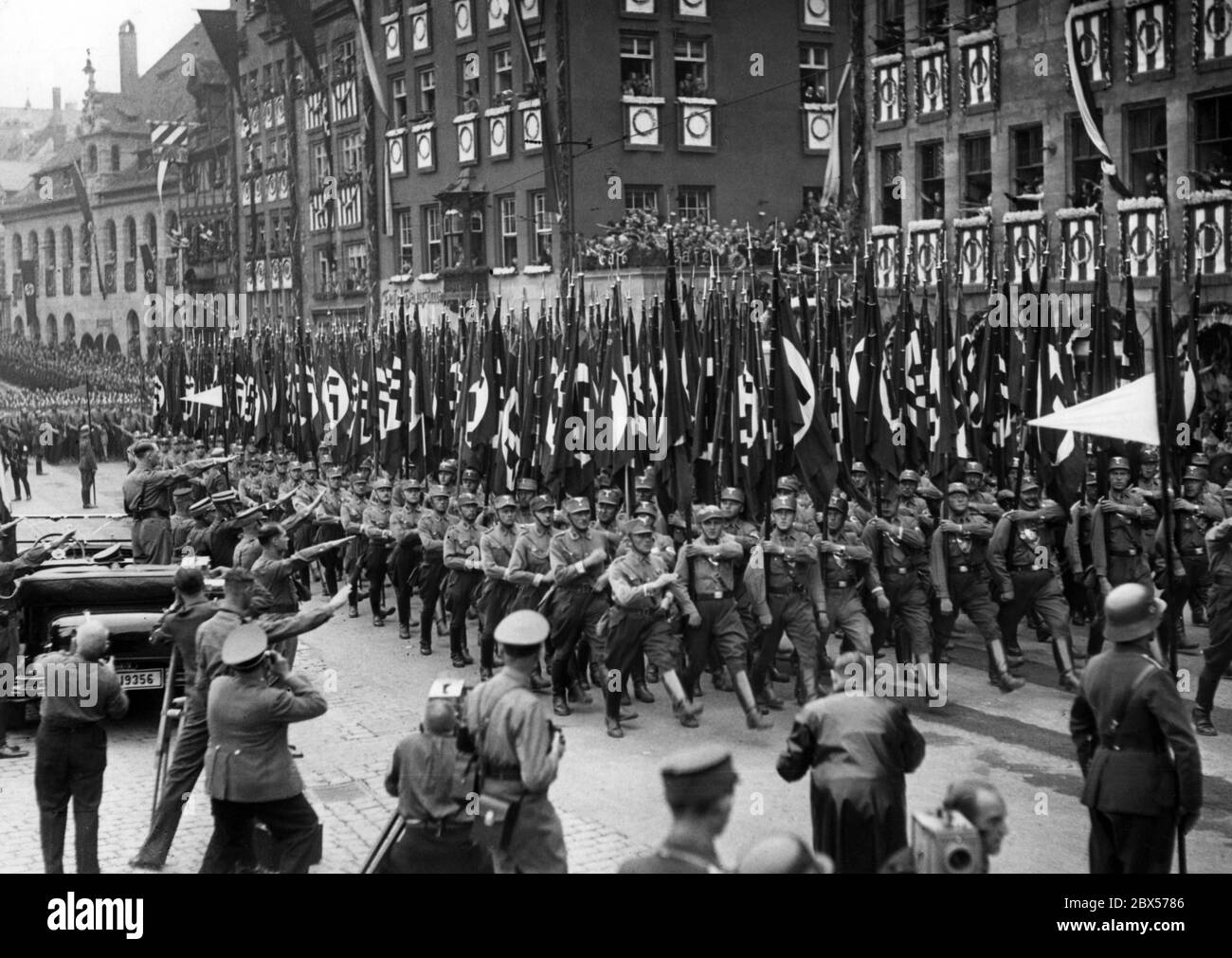 Adolf Hitler, der in seinem Mercedes steht, nimmt den Gruß der marschierenden SA-Fahnenträger auf dem Nürnberger Hauptmarkt, dem sogenannten Adolf-Hitler-Platz. Vor ihm von rechts: Rudolf Hess, Viktor Lutze, Adolf Huehnlein und andere. Im Vordergrund stehen mehrere Fotografen. Stockfoto