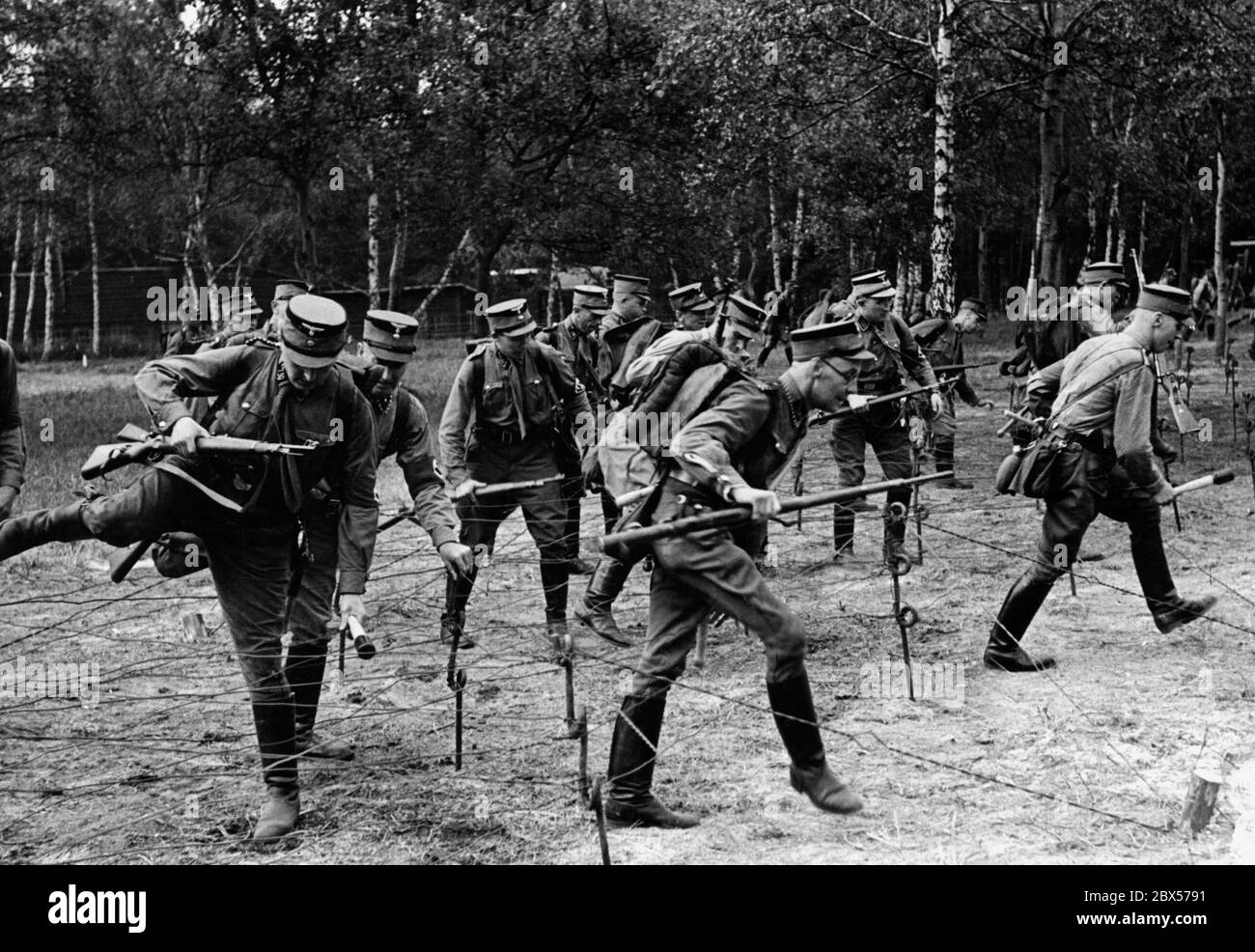 Wettbewerb der SA Wehrmannschaft Berlin Brandenburg. Die Teilnehmer überwinden mit ihrem Gepäck und Mauser K98 in den Händen nur das Drahthindernis 'Spanish Rider'. Dies geschieht auf der Militärbahn an den Postfenn im Grünewald. Stockfoto