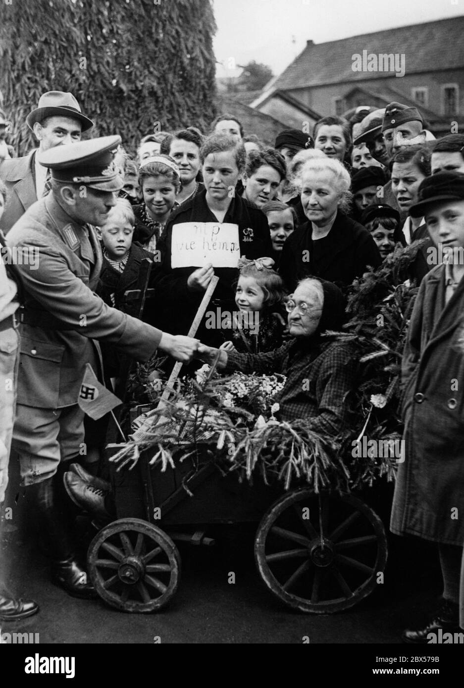 Eine alte Frau kehrt mit ihrer Familie nach Saarbrücken Herrensohr zurück. Ein Funktionär der NSDAP gratuliert ihr. Stockfoto