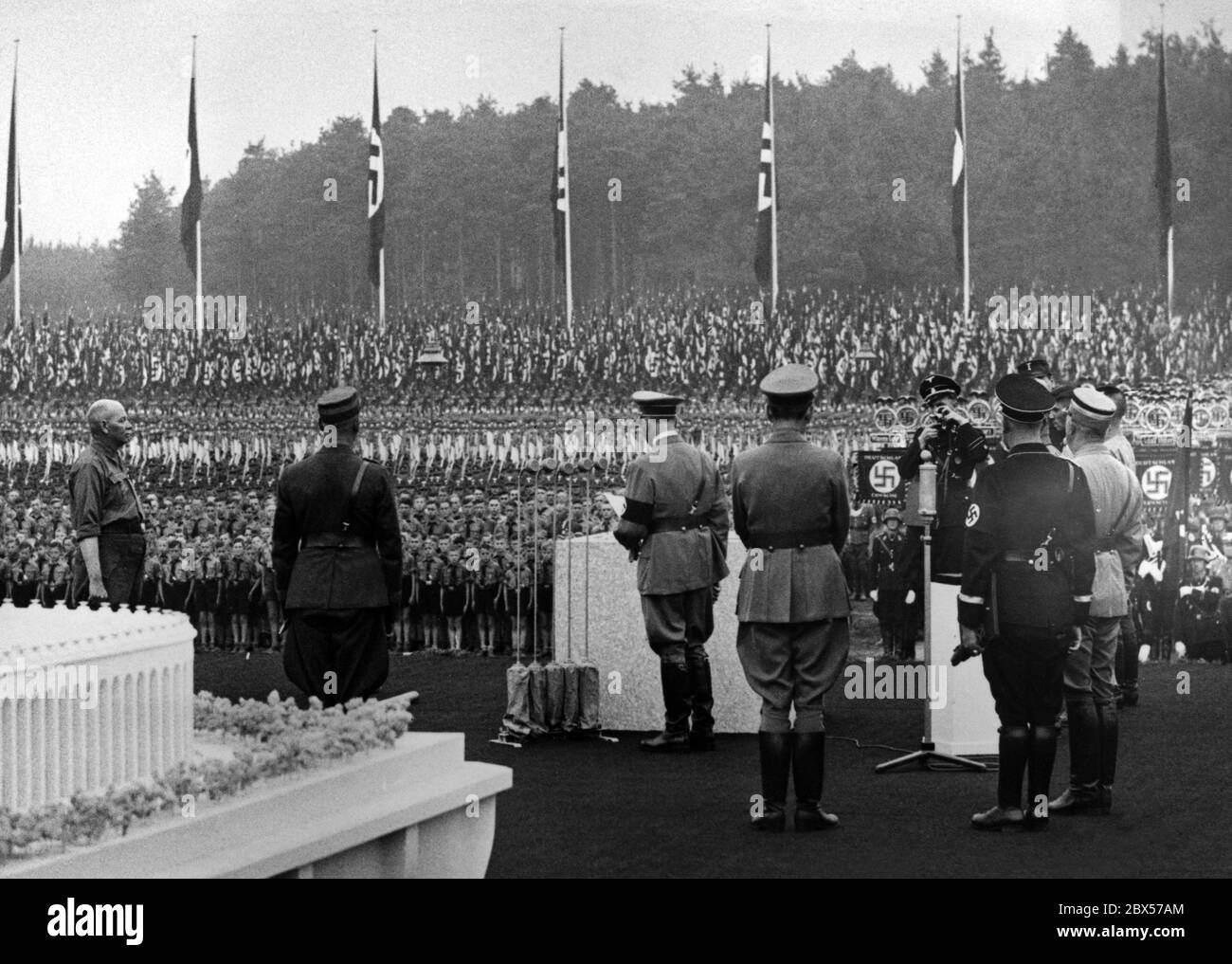 Auf dem Reichsparteitagsgelände in Nürnberg hält Adolf Hitler anlässlich der Grundsteinlegung des Deutschen Stadions (der Grundstein befindet sich rechts neben Hitler, ein Modell links) eine Rede zu den teilnehmenden Formationen der Hitlerjugend, RAD, SA UND SS. Stockfoto