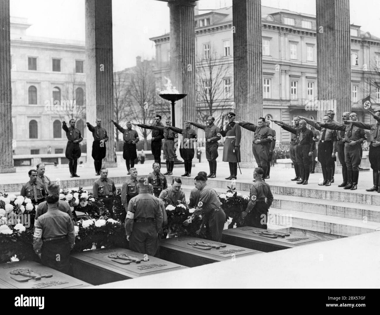 Nach dem traditionellen marsch in die Feldherrenhalle legt Adolf Hitler in einem Ehrentempel auf dem Münchener Königsplatz einen Kranz für die Gefallenen des Hitler-Ludendorff-Putsches. Oben mit Nazi-Gruß sind wahrscheinlich von links nach rechts zu sehen: Hanns Bunge (1. V. l.), Max Amann (3. V. l.), Wilhelm Frick (5. V. l.), Ulrich Graf (6. V. l.), Werner von Blomberg (8. V. l.), Hermann Göring, Adolf Wagner, Hans Frank, Julius Streicher, Heinrich Himmler, Hermann Kriebel, Alfred Rosenberg und Karl Fiehler. Im Hintergrund ist das Brown House. Stockfoto