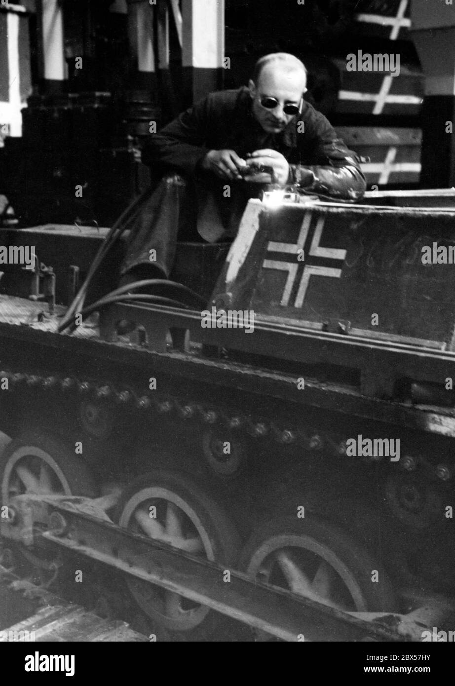 Ein Arbeiter schweißen auf einem Kettenfahrzeug, auf dem sich ein Balkenkreuz der Wehrmacht befindet. Stockfoto