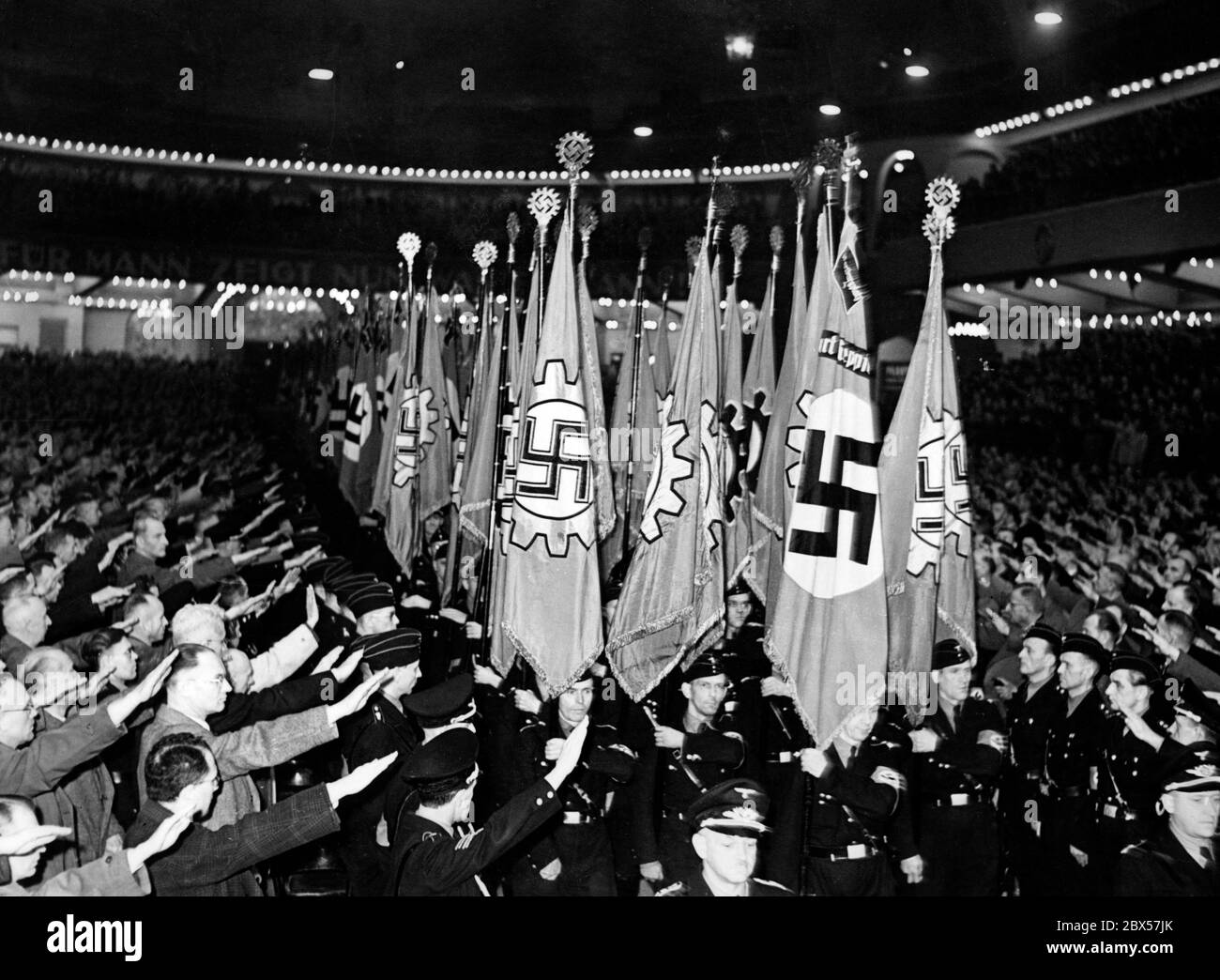 Parade der Fahnenträger während eines Firmenaufrufs der Deutschen Arbeitsfront (DAF) im Sportpalast Berlin. Gezeigt werden Hakenkreuzfahnen mit DAF-Logo sowie spezielle Modellpflanzenfahnen, die durch die DAF verloren gegangen sind. Mit Hilfe von Aufforderungen und Fahnenmärschen versucht die Deutsche Arbeitsfront (DAF), die Loyalität und Beharrlichkeit der Angestellten während des Nationalsozialismus zu wecken. Stockfoto