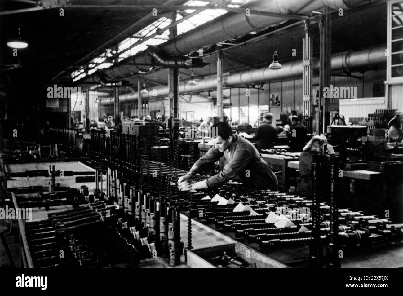 Die Komponenten für das MG34 werden in einem Fabrikgebäude gefertigt. Auf dem Bild befestigt ein Arbeiter eine Steuerkarte an fertigen und geprüften Teilen. Stockfoto