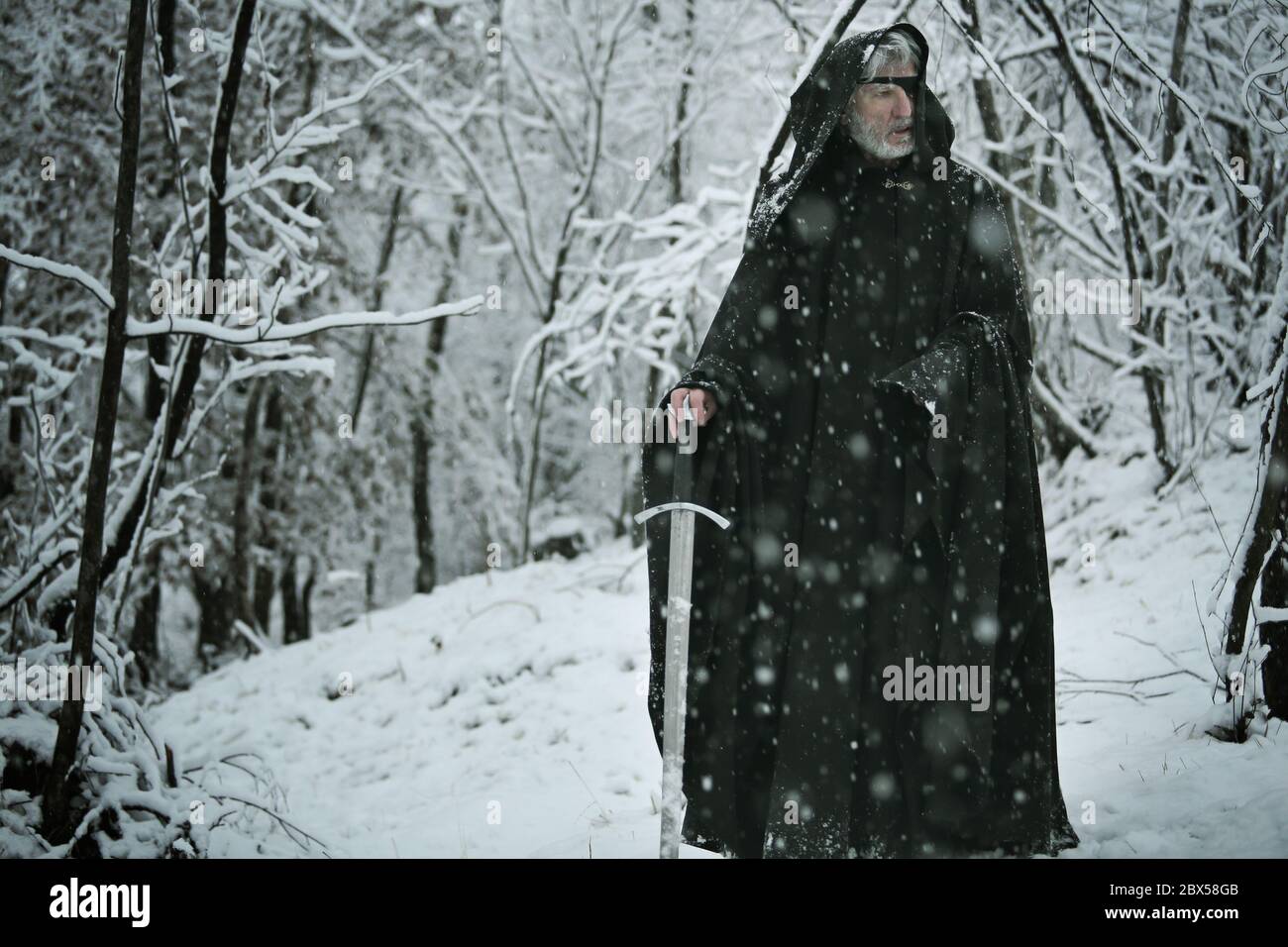Geheimnisvoller alter Mann geht mit einem Schwert in verschneiten Wald. Mythos und Fantasie Stockfoto