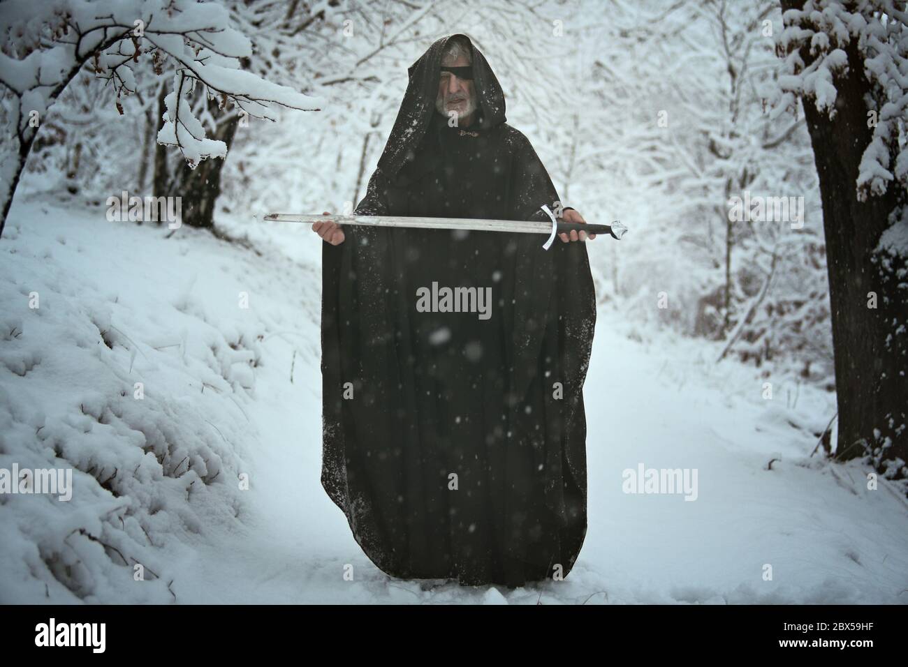 Ein Augen geheimnisvollen alten Mann bietet ein Schwert in verschneiten Wald. Mythos und Fantasie Stockfoto