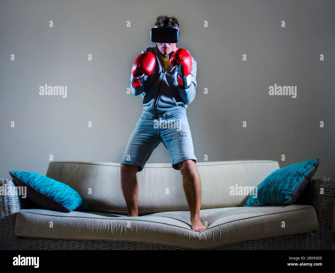 Junge Gamer Mann mit VR-Brille Kopfbedeckung und Boxhandschuhe spielen Simulator 3D Kampf Videospiel Spaß auf der Sofa-Couch zu Hause genießen spannende virt Stockfoto