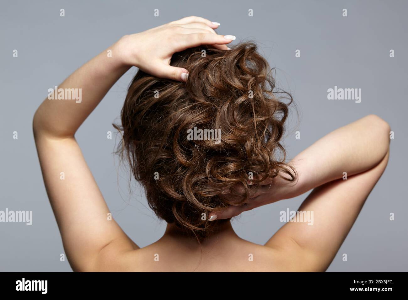 Rückansicht Porträt von schönen jungen dunklen Brünette Frau. Weiblich mit kreativer Frisur auf grauem Hintergrund. Stockfoto