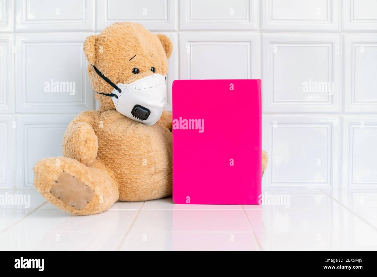 Teddybär mit Gesichtsmaske und rosa Notizbuch auf weißem Hintergrund. Konzept der Heimschule, Isolation. Zu Hause bleiben. Corona-Virus. Stockfoto