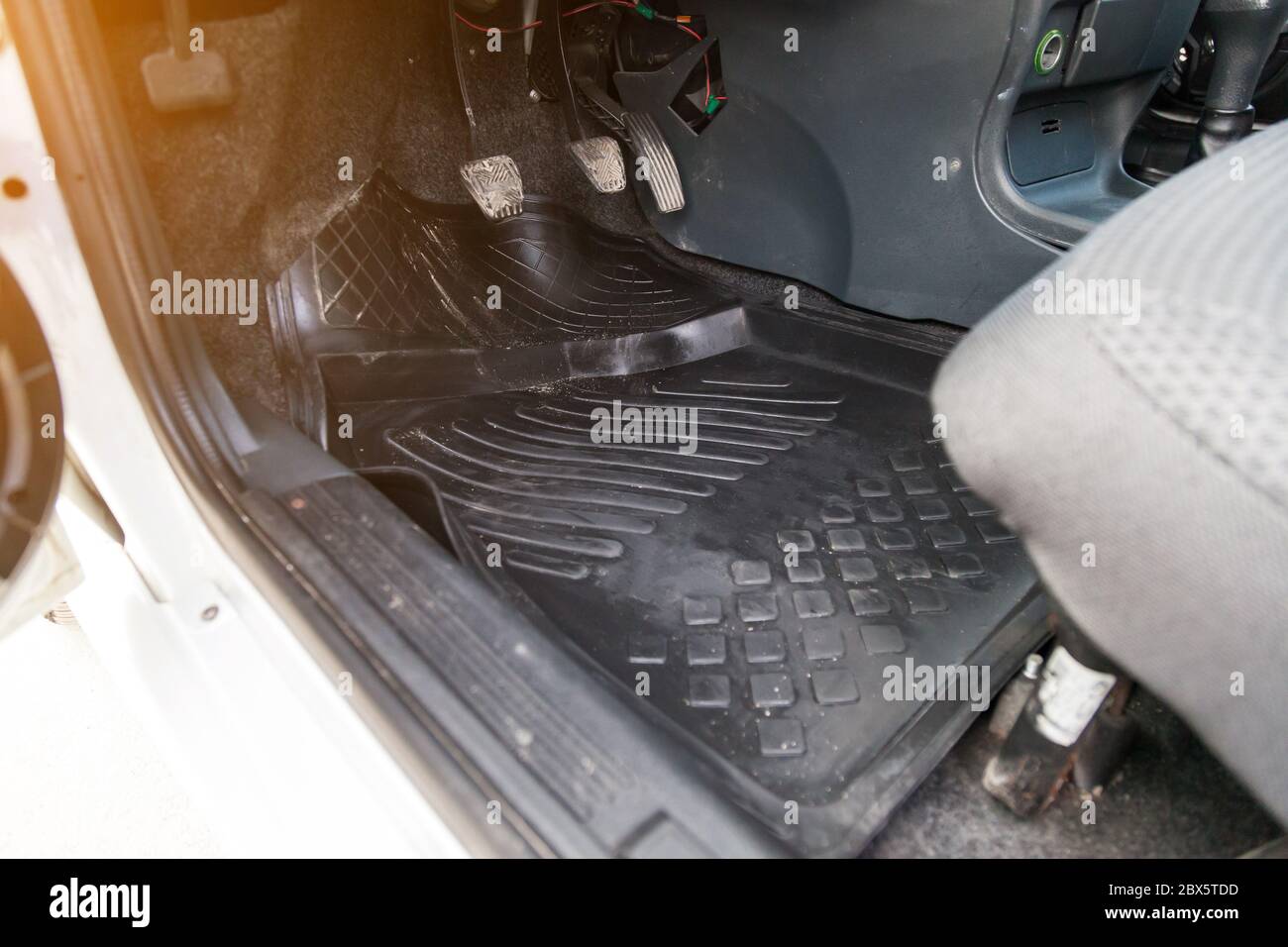 Öffnen Sie die Fahrertür Nahaufnahme des schmutzigen Gummiteppichs unter den Füßen mit Gas-, Brems- und Kupplungspedalen vor einem Trockenreiniger in einer Autowaschanlage. Stockfoto