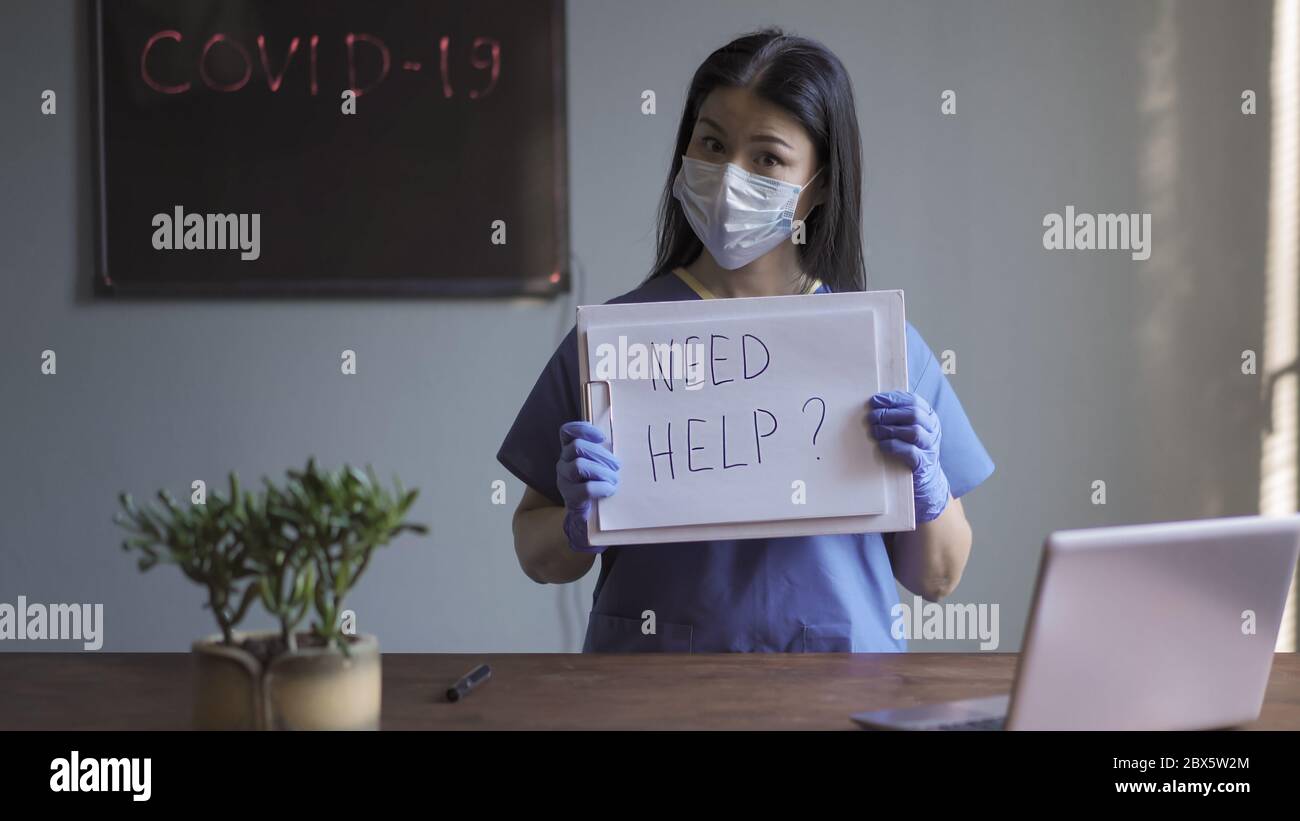 Ärztin fragt sich, ob Hilfe benötigt wird, wenn man die Kamera fragend anschaut. Asiatische Frau in medizinischer Uniform im Büro vor dem Hintergrund der Stockfoto