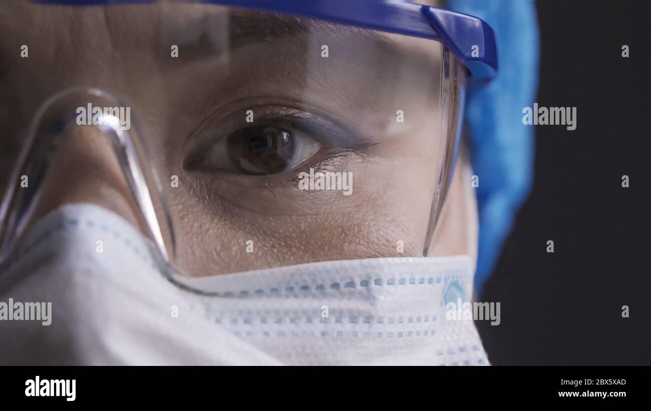 Schönes Auge eines müden Arztes, der eine Schutzbrille trägt. Asiatische Frau in Schutzbrille und Maske Blick auf Kamera. Nahaufnahme Stockfoto