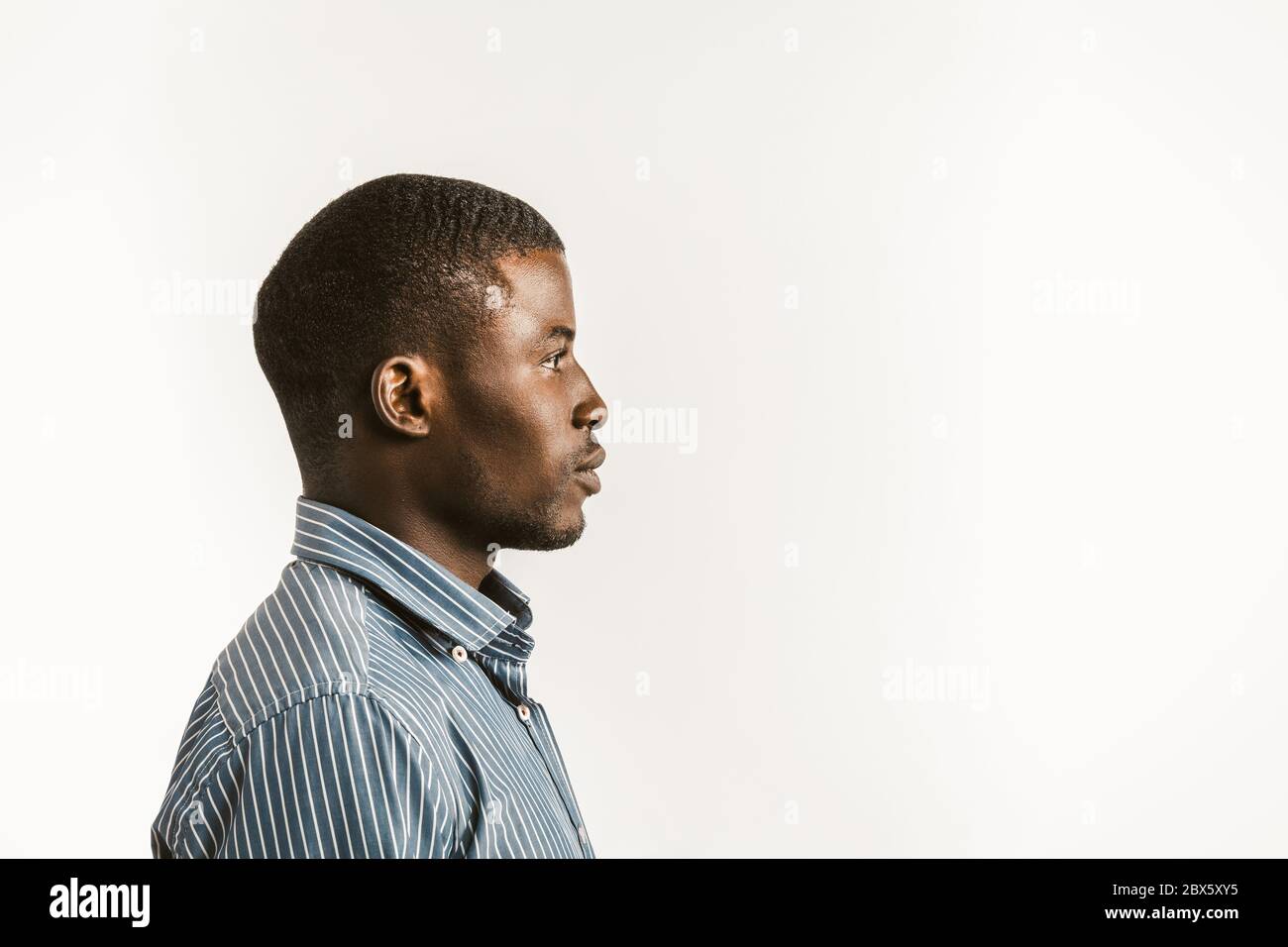 Junger Afrikaner auf weißem Hintergrund. Profilansicht eines ernsthaften afro-amerikanischen Studenten oder Geschäftsmannes, der auf der rechten Seite mit Textraum oder Textraum schaut Stockfoto