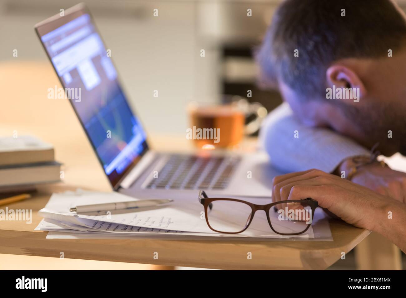 Verschwommener, müder junger kaukasischer Mann mit Brille in der Hand, einschlafen nach der Arbeit am Laptop, am Schreibtisch schlafen, auf Brille konzentrieren, Stockfoto
