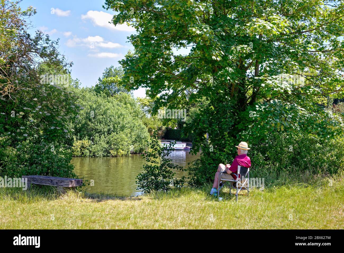 Ein eleganter und gut gekleideter älterer Herr, der an einem heißen Sommertag in Surrey England auf einem Sitz an der Themse in Runnymede sitzt Stockfoto