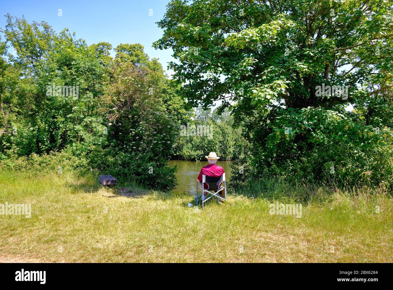 Ein eleganter und gut gekleideter älterer Herr, der an einem heißen Sommertag in Surrey England auf einem Sitz an der Themse in Runnymede sitzt Stockfoto